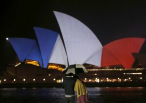 A couple stands in the rain as the blue, white and red colours of France's national flag are projected onto the sails of Sydney's Opera House in Australia November 14, 2015 following the attacks in Paris.    REUTERS/Jason Reed - RTS6YZW